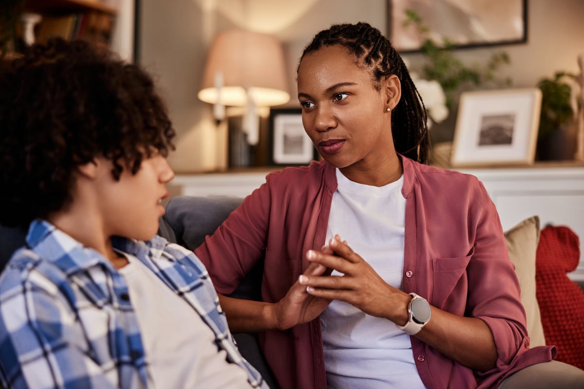 Adult mentor sitting with a young person on a couch, talking together in a relaxed mentoring conversation, both faces fully visible