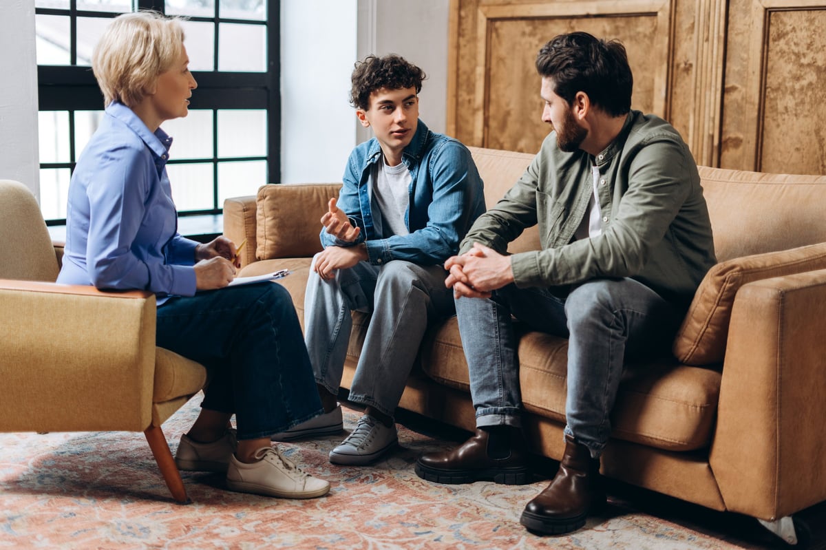 Youth worker sitting with a teenager having a positive, supportive conversation in an office, both faces fully visible in a calm and encouraging setting