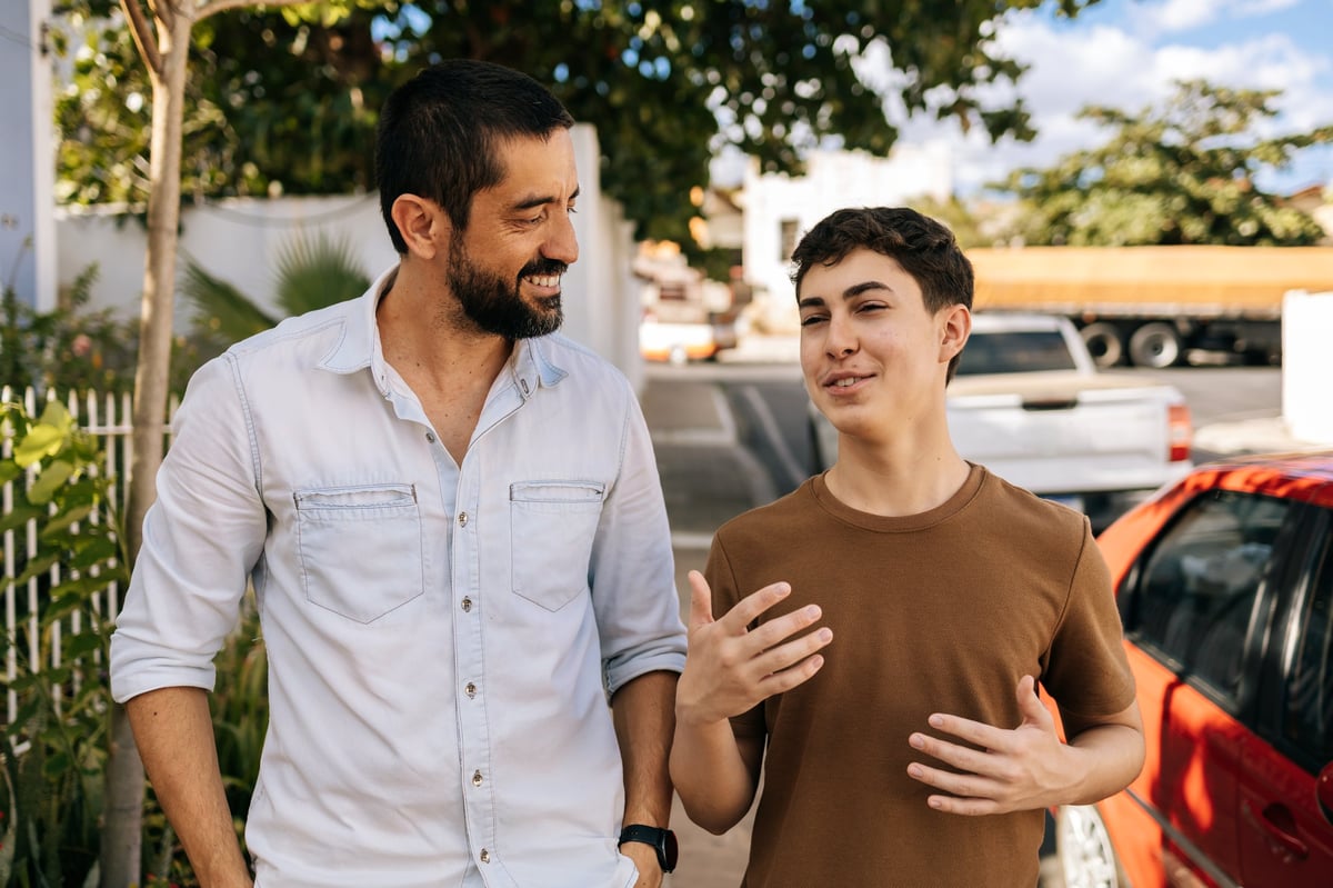 Father and son talking during an outdoor walk, both faces fully visible, with attentive listening and encouraging guidance in a relaxed community setting